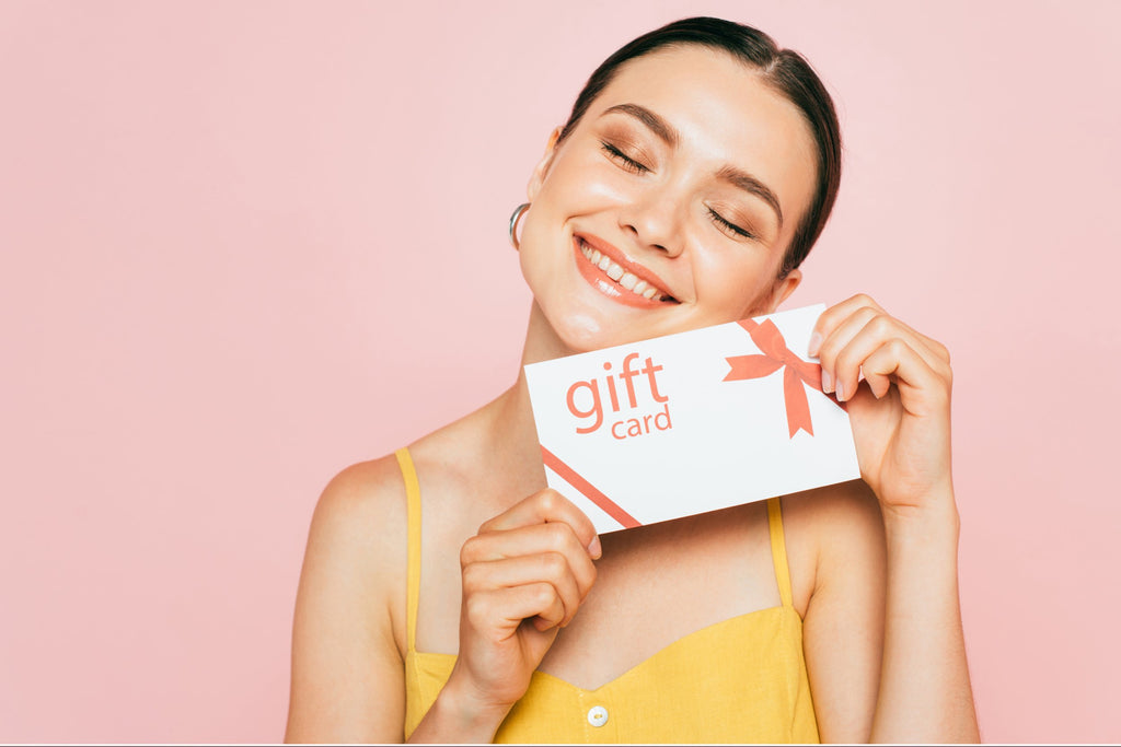 Smiling lady holding a gift card against pink backdrop